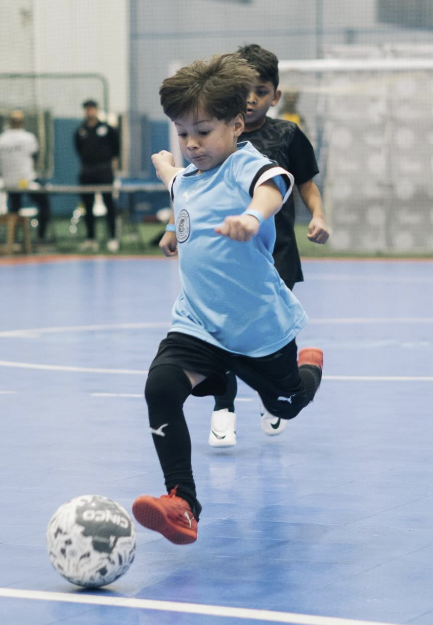 Youth futsal player in Cadence blue jersey dribbling the ball